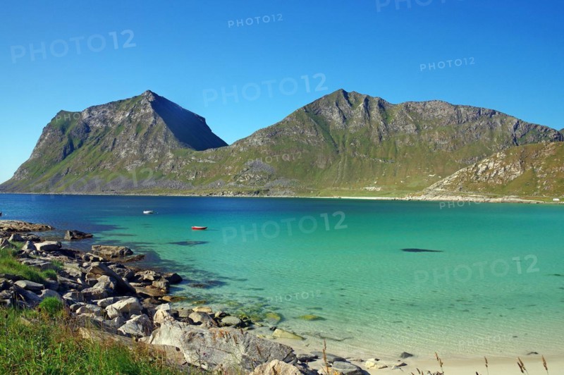 Crystal clear sea bay with small boat and rugged green mountains
