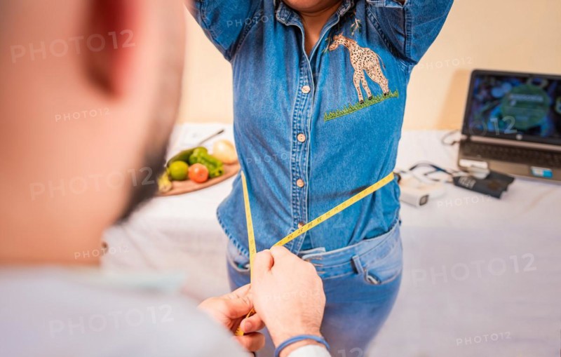 Close-up of nutritionist measuring waist to patient. View of a male nutritionist measuring female patient waist. Concept of weight loss and professional nutritionist