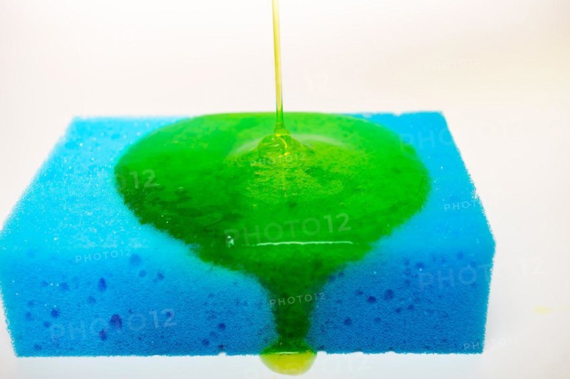 Green liquid soap dripping on a blue sponge on a white background