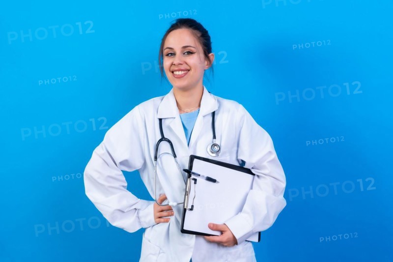 Portrait of smiling female doctor in medical gown standing isolated on blue