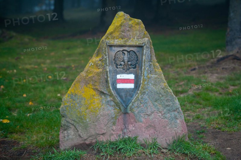 A large obelisk is placed next to the tourist trail with a trail sign and an eagle on it. Polish mountains