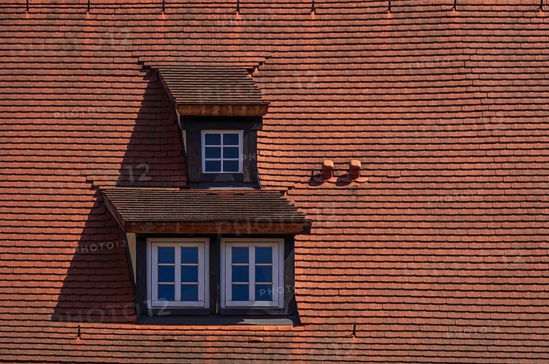 Three dormers with mansard windows in a roof structure covered with red tiles
