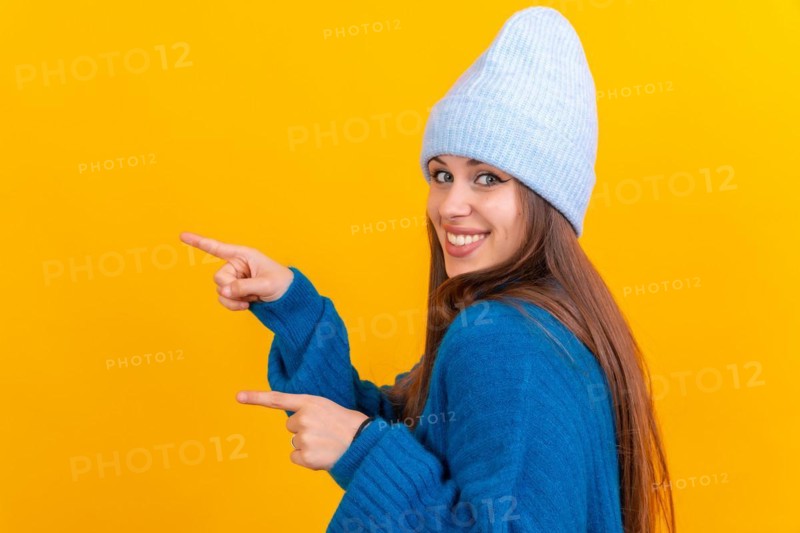 Attractive woman smiling pointing fingers at copy space on yellow background