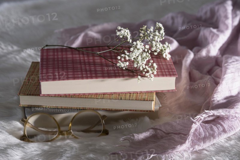 Three closed books with glasses and babys breath on white fur with pink cloth
