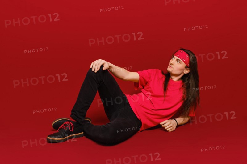Active young man with long hair and head band sitting on floor in red studio