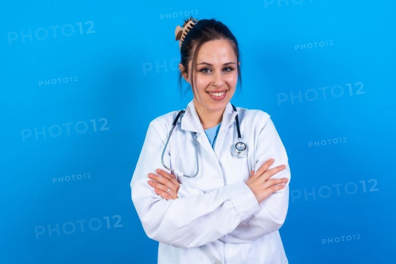 Portrait of smiling female doctor in medical gown standing isolated on blue