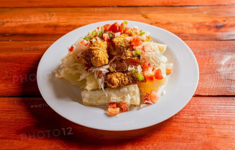 Traditional chicharron dish with cassava and tomato salad. Latin food chicharron con yuca served on wooden table. Nicaraguan dish chicharron with cassava on the table