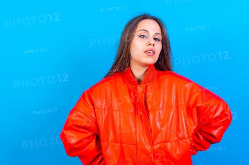 Close up portrait of young caucasian woman in red windbreaker isolated on blue background
