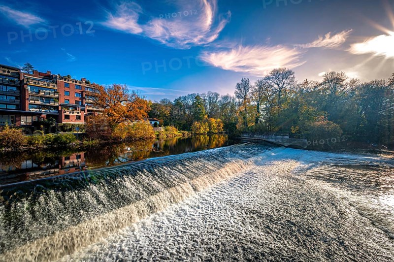 The Leineinsel waterfall next to the Leineinsel residential area in the district of Doehren in autumn with veil clouds