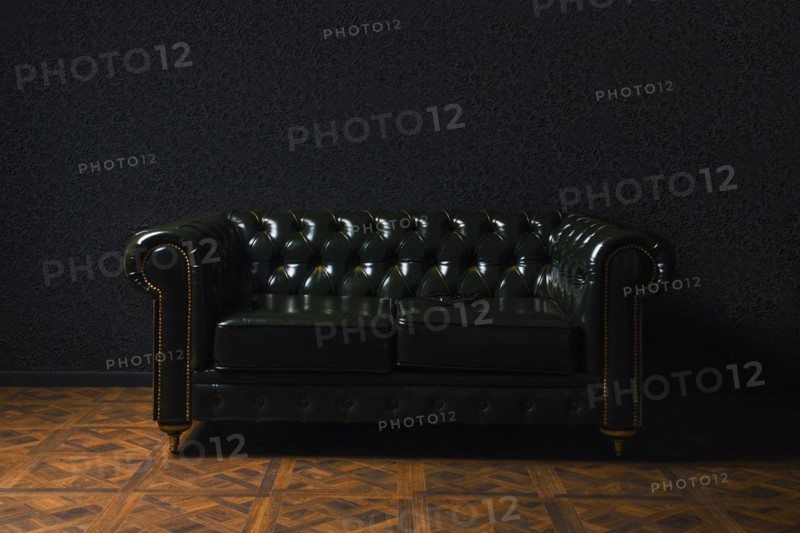 Glossy green leather couch next to black wall