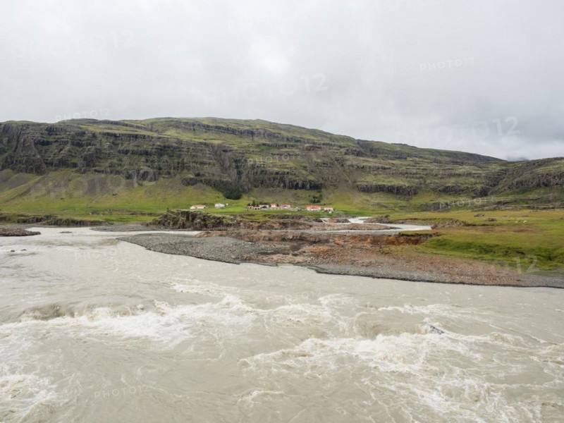 Glacier river and farm in front of mountain range
