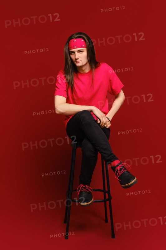 Young adult man sits on high stool with his leg on another leg and leaning forward