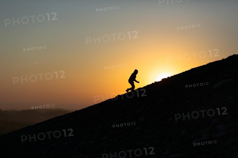 Silhouette of man is climbing to peak of hill with sunset or sunrise background. Poland