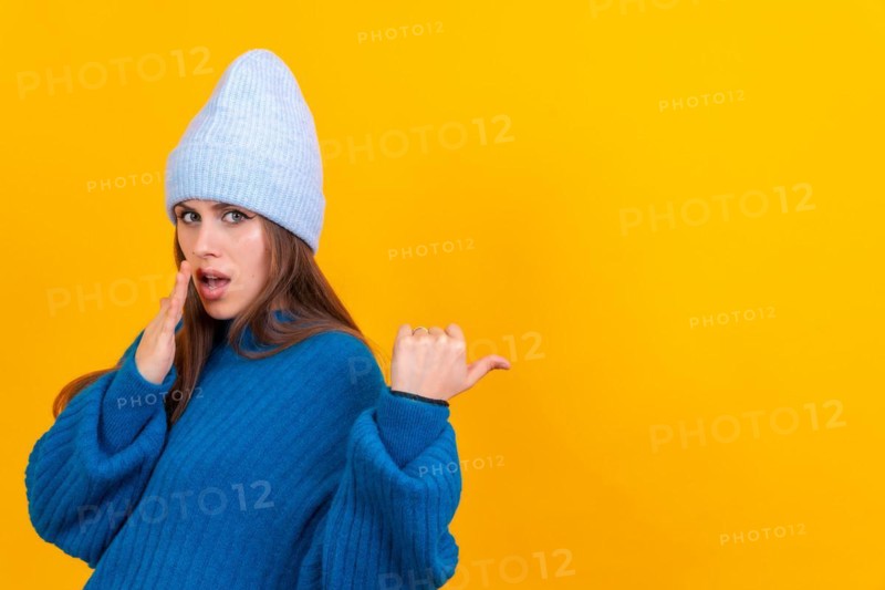 Attractive woman smiling pointing fingers at copy space on yellow background