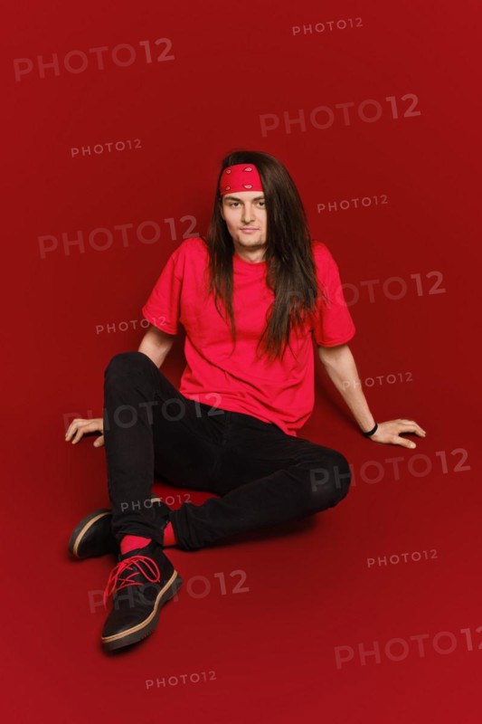 Active young man with long hair and head band sitting on floor in red studio