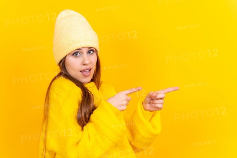 Attractive woman smiling pointing fingers at copy space on yellow background