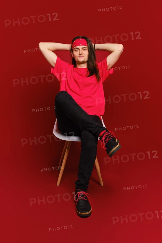 Man threw his hands behind his head and sits relaxed on chair in red studio