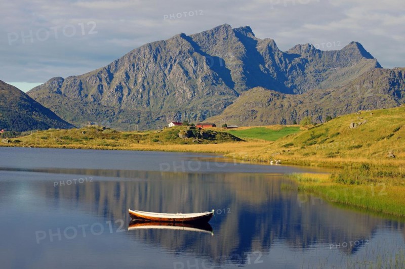 Small wooden rowboat and high barren mountains reflected in the calm waters of a small lake