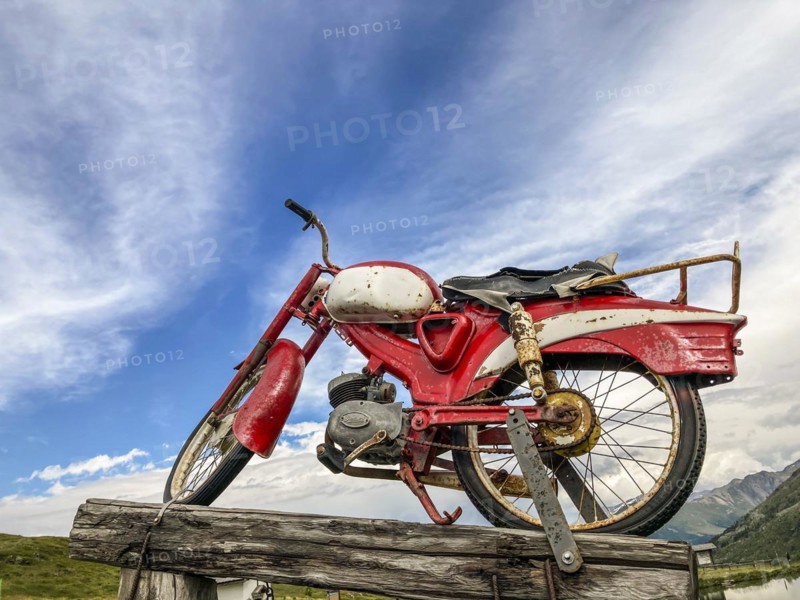 An old rusty red motorcycle stands on a wooden pole