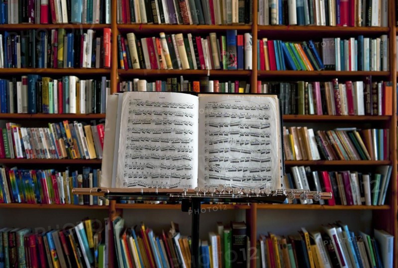 Sheet music and flute on a music stand in front of a wall of books