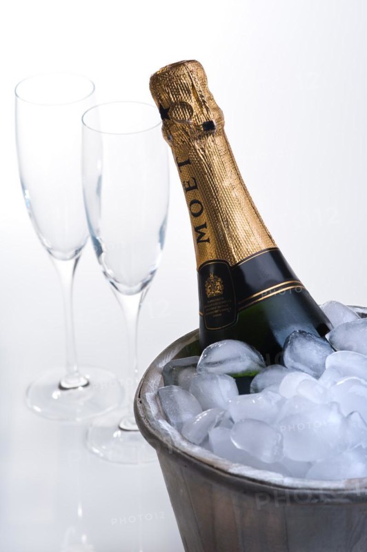 Bottle of champagne in ice bucket full of ice and two empty champagne flutes