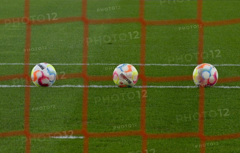 Three adidas Derbystar match balls lie on turf behind goal net