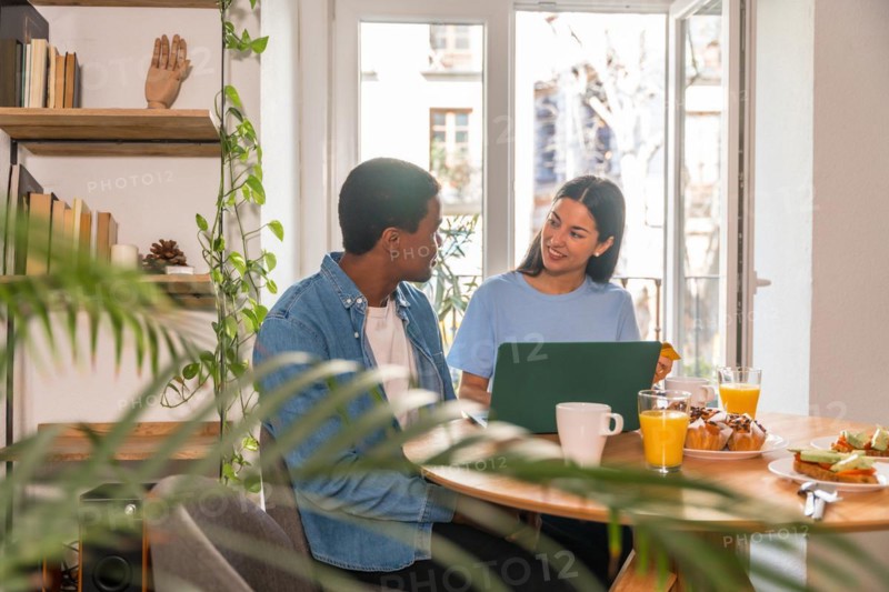 Couple making purchase online with the computer while having breakfast, next to the window, buying flights