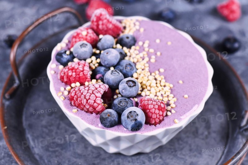 Fruit smoothie bowl with yogurt decorated with healthy raspberry, blueberry and puffed quinoa grain on iron tray