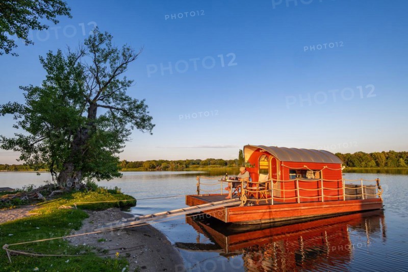 Man sitting on a houseboat, house raft, in front of the island Kiehnwerder, Breitlingsee, Brandenburg an der Havel, Havelland, Brandenburg, Germany, Europe