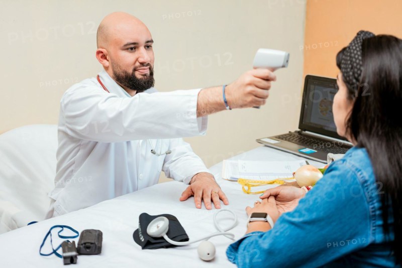 Doctor measuring temperature with infrared gun to female patient, Doctor taking temperature to woman patient in office, Male doctor taking temperature with gun to patient
