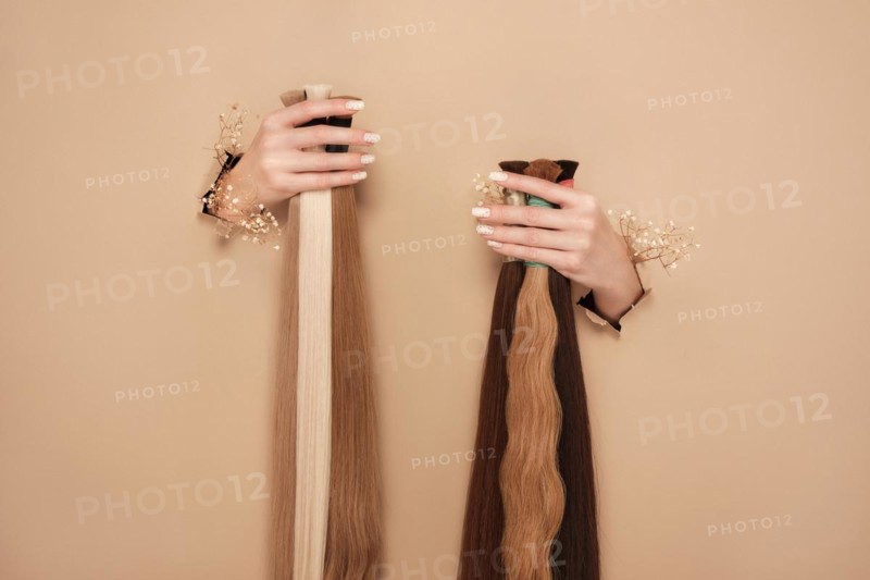 Hands with flowers hold strands of hair for extensions on a beige background. hair beauty
