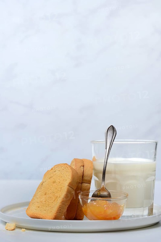 Rusk, glass of milk and orange marmalade in small bowls
