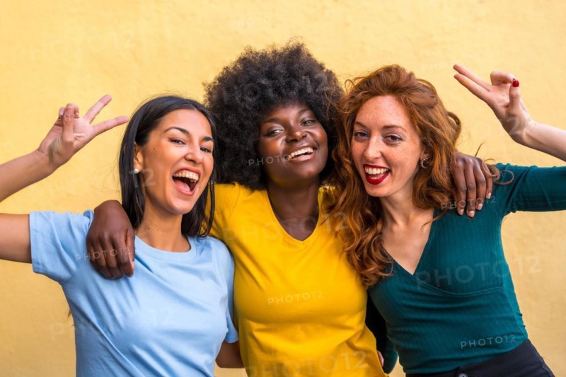 Portrait of beautiful multiethnic female friends smiling on a yellow wall having fun