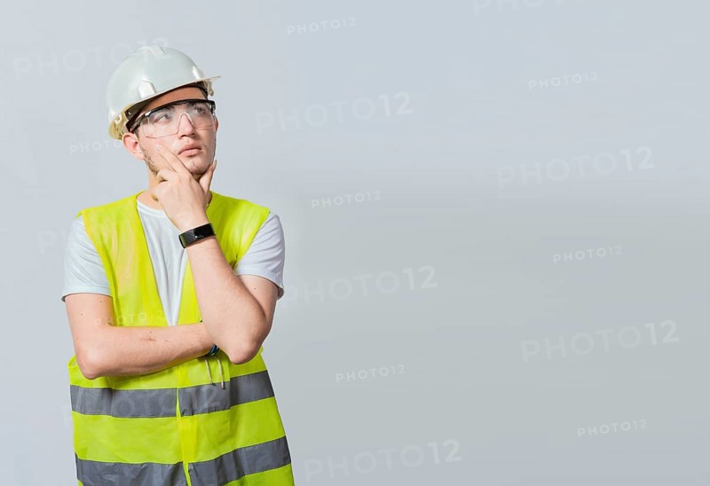 Concept of a meditative engineer solated. Pensive builder man with hand on chin, Portrait of young builder thinking with hand on chin isolated, A pensive engineer on white background