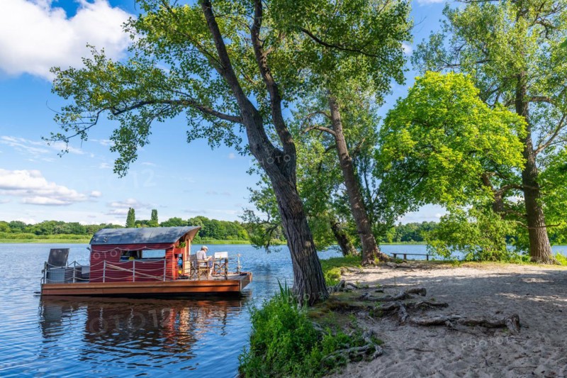 Man sitting on a houseboat, house raft, in front of the island Kiehnwerder, Breitlingsee, Brandenburg an der Havel, Havelland, Brandenburg, Germany, Europe