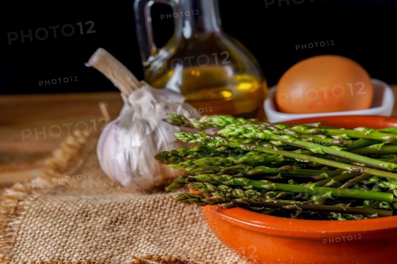 Close-up of wild asparagus in an earthenware casserole with olive oil, eggs and garlic black background