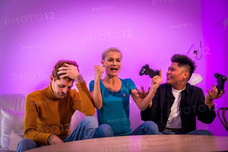 Group of young friends playing video games together on the sofa at home, purple led, woman winning