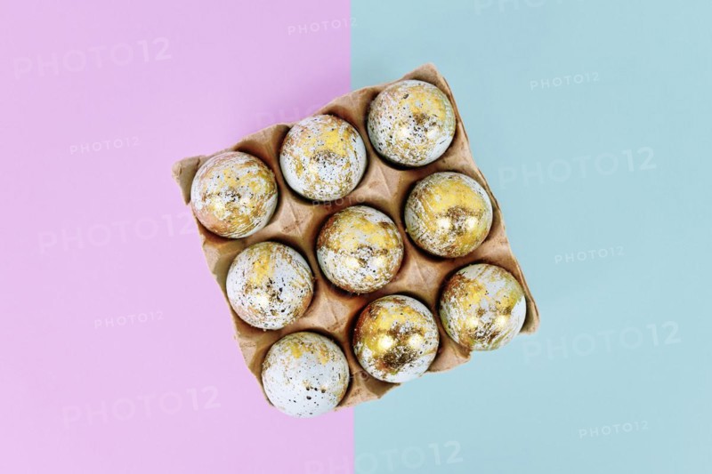 Painted Easter eggs with golden spots in egg carton on blue and violet background
