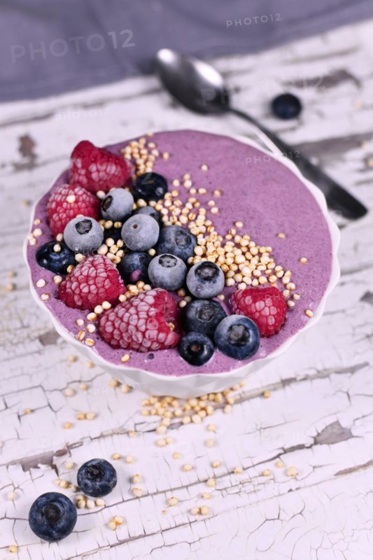 Fruit smoothie bowl with yogurt decorated with healthy raspberry, blueberry and puffed quinoa grain on iron tray