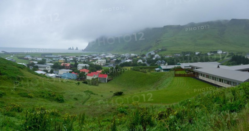 Village view of Vik in the rain, lava beach with Reynisdrangar rock needles in the back, Vik, Iceland, Europe