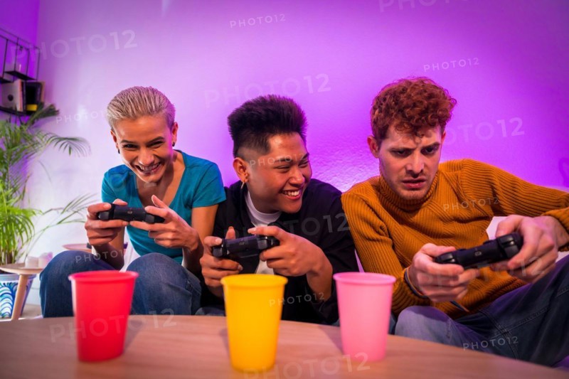 Group of young friends playing video games together on the sofa at home, smiling, young millennials