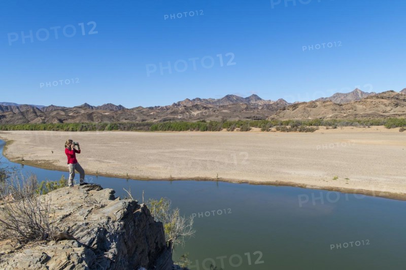 Woman taking pictures at the Orange River, also known as the Orange River, on the border between Namibia and South Africa, Oranjemund, Sperrgebiet National Park, also known as Tsau ÇKhaeb National Park, Namibia, Africa