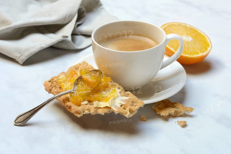 Orange marmalade in small bowls and on crispbread and cup of coffee