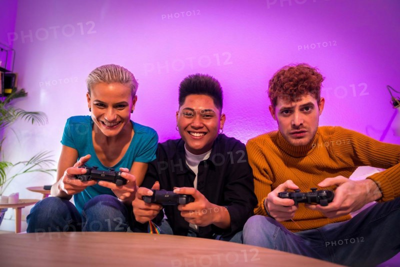 Group of young friends playing video games together on the sofa at home, portrait looking at camera