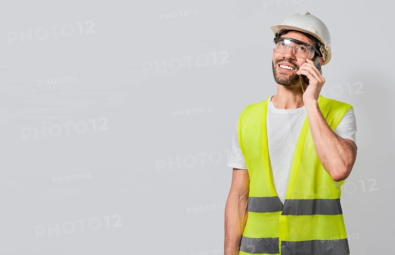Smiling engineer talking on the phone isolated with copy space. Young builder engineer in vest talking on cell phone isolated. Civil engineer concept talking on cellphone isolated