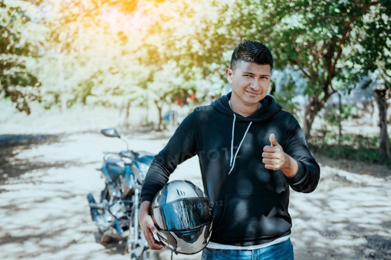 Portrait of motorcyclist holding safety helmet with thumb up. Smiling motorcyclist man holding safety helmet on the road. Motorcyclist giving thumbs up holding safety helmet on the road