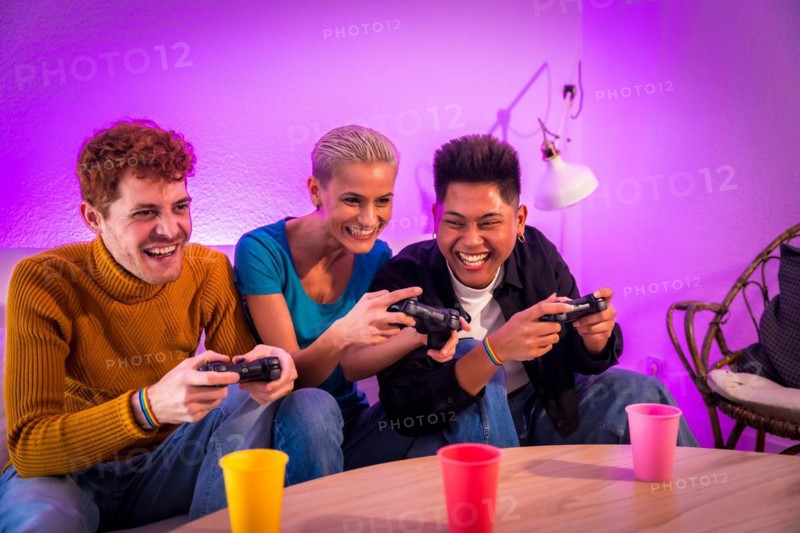 Group of young friends playing video games together on the sofa at home, purple led, having fun