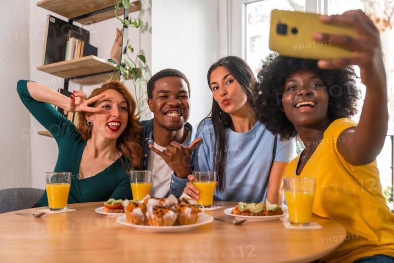 Multiethnic friends at a breakfast with orange juice and muffins at home, taking a selfie