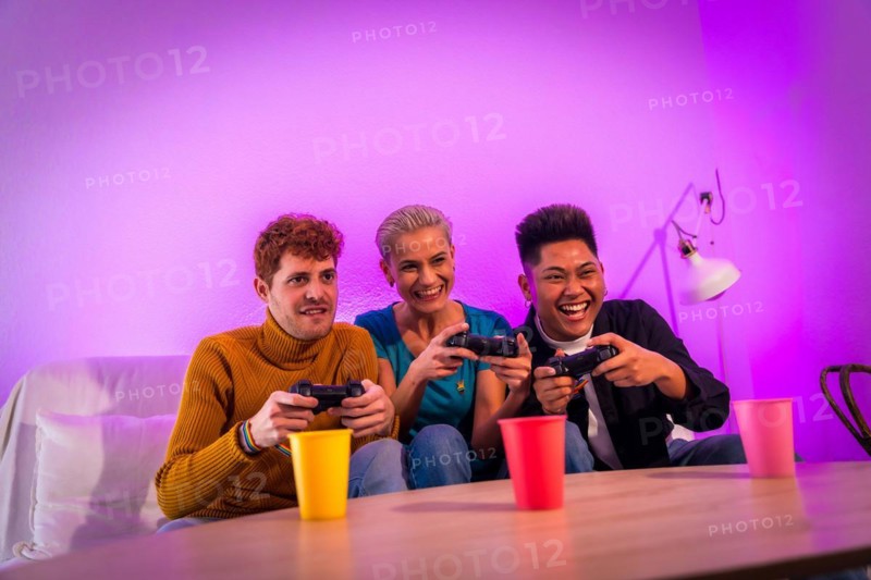 Group of young friends playing video games together on the sofa at home, purple led, racing game