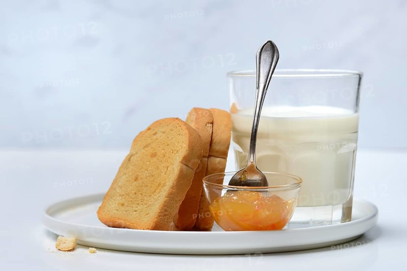 Rusk, glass of milk and orange marmalade in small bowls